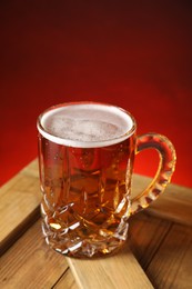 Mug with fresh beer on wooden crate against red background