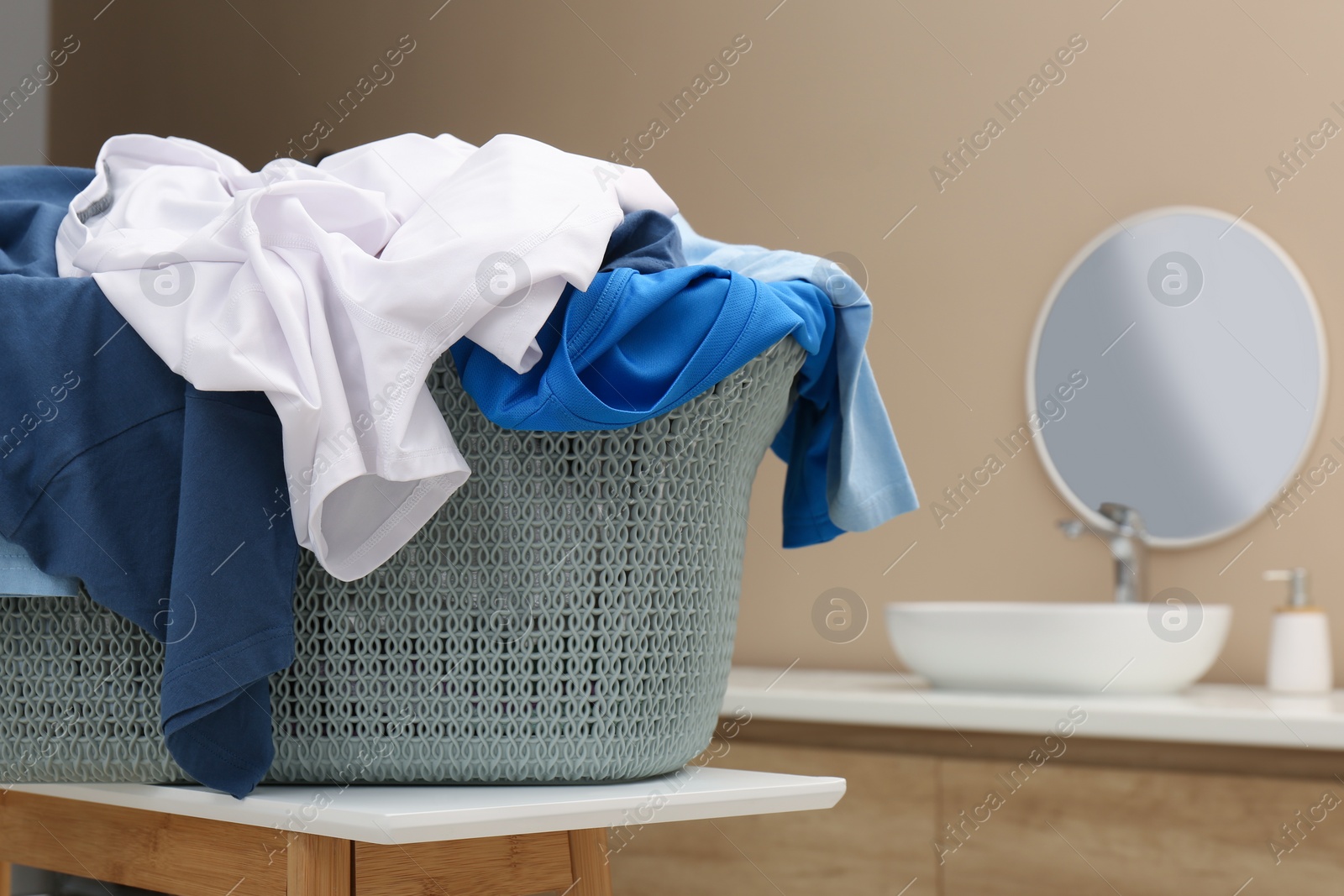 Photo of Plastic laundry basket overfilled with clothes on white table in bathroom. Space for text