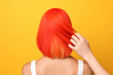 Professional stylist and young woman with bright dyed hair on orange background, back view