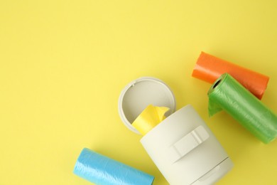 Photo of Dog waste bags and dispenser on yellow background, flat lay. Space for text