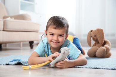 Cute child imagining himself as doctor while playing with stethoscope and toy at home