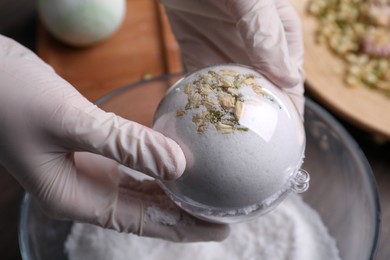 Photo of Woman in gloves making bath bomb at table, closeup