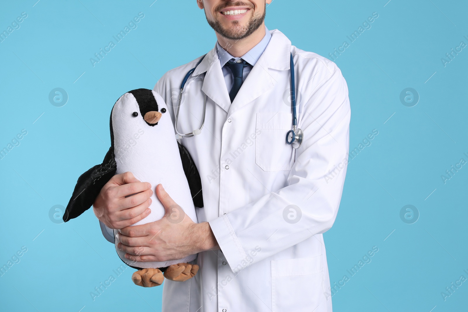 Photo of Pediatrician with toy penguin and stethoscope on light blue background, closeup