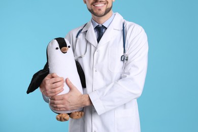 Photo of Pediatrician with toy penguin and stethoscope on light blue background, closeup