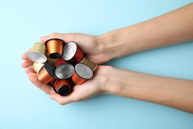 Woman holding heap of coffee capsules on light blue background, top view