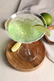 Photo of Delicious Margarita cocktail with ice cubes in glass and lime on light table