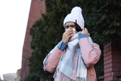 Photo of Woman with tissue blowing runny nose outdoors. Cold symptom