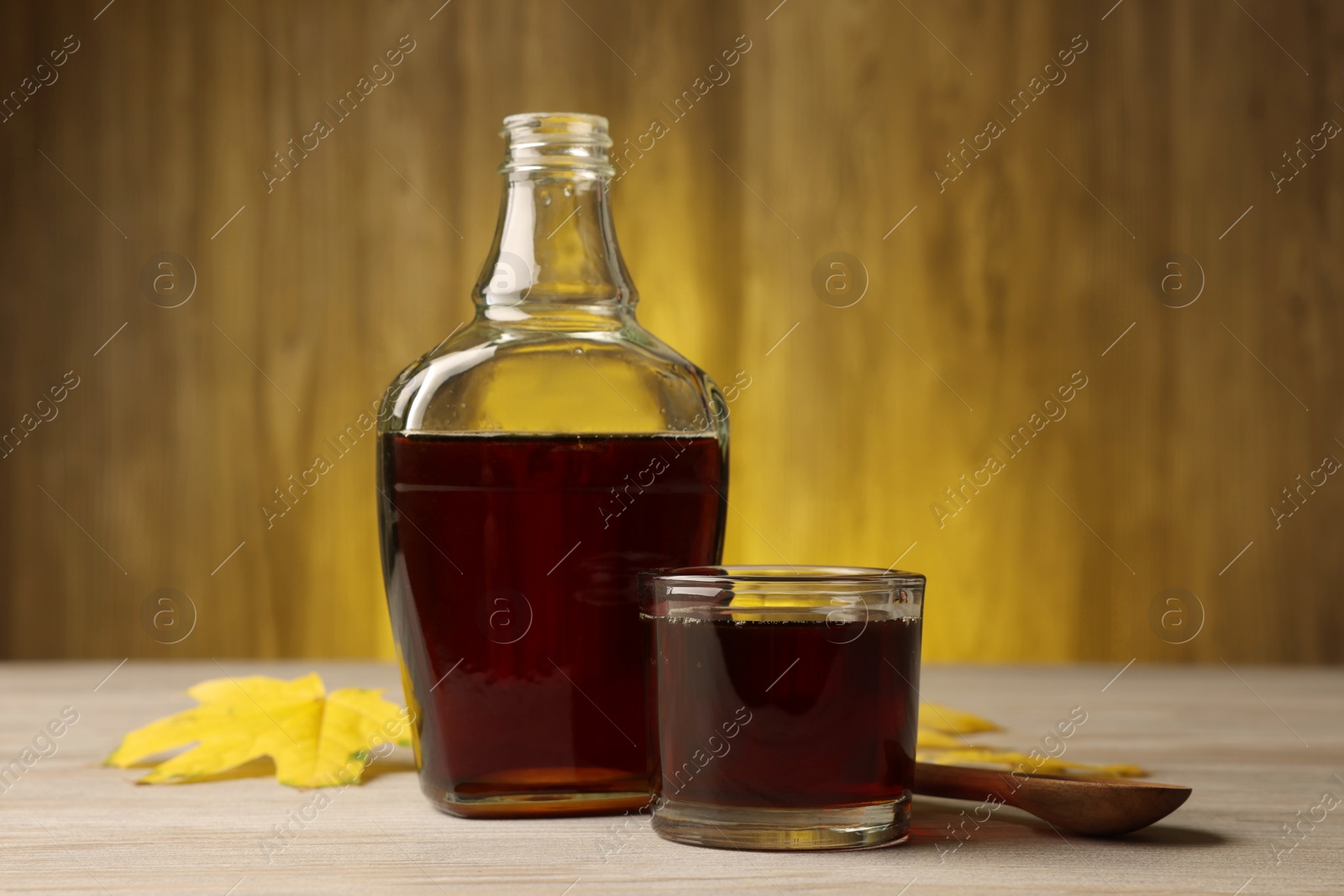 Photo of Tasty maple syrup, spoon and leaves on wooden table