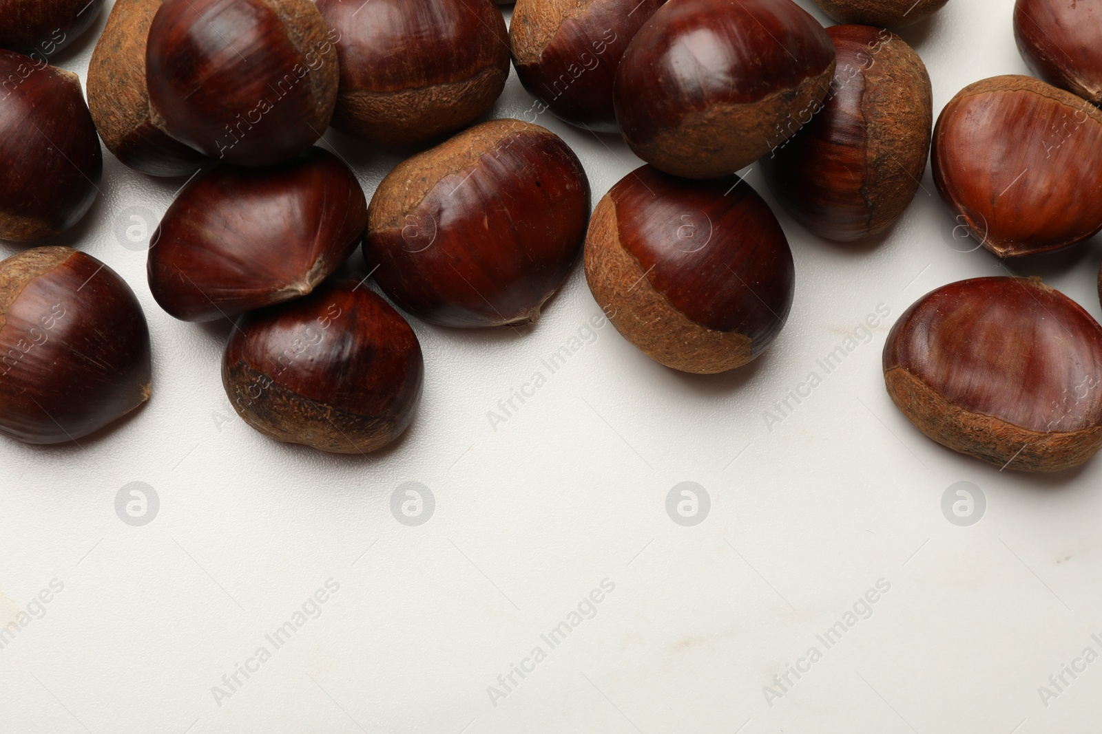 Photo of Sweet fresh edible chestnuts on white marble table, top view. Space for text