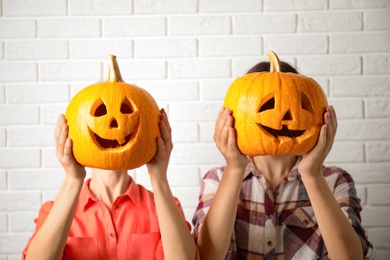 Photo of Women with pumpkin heads near white brick wall. Jack lantern - traditional Halloween decor