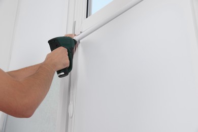 Photo of Worker installing roller window blind indoors, closeup
