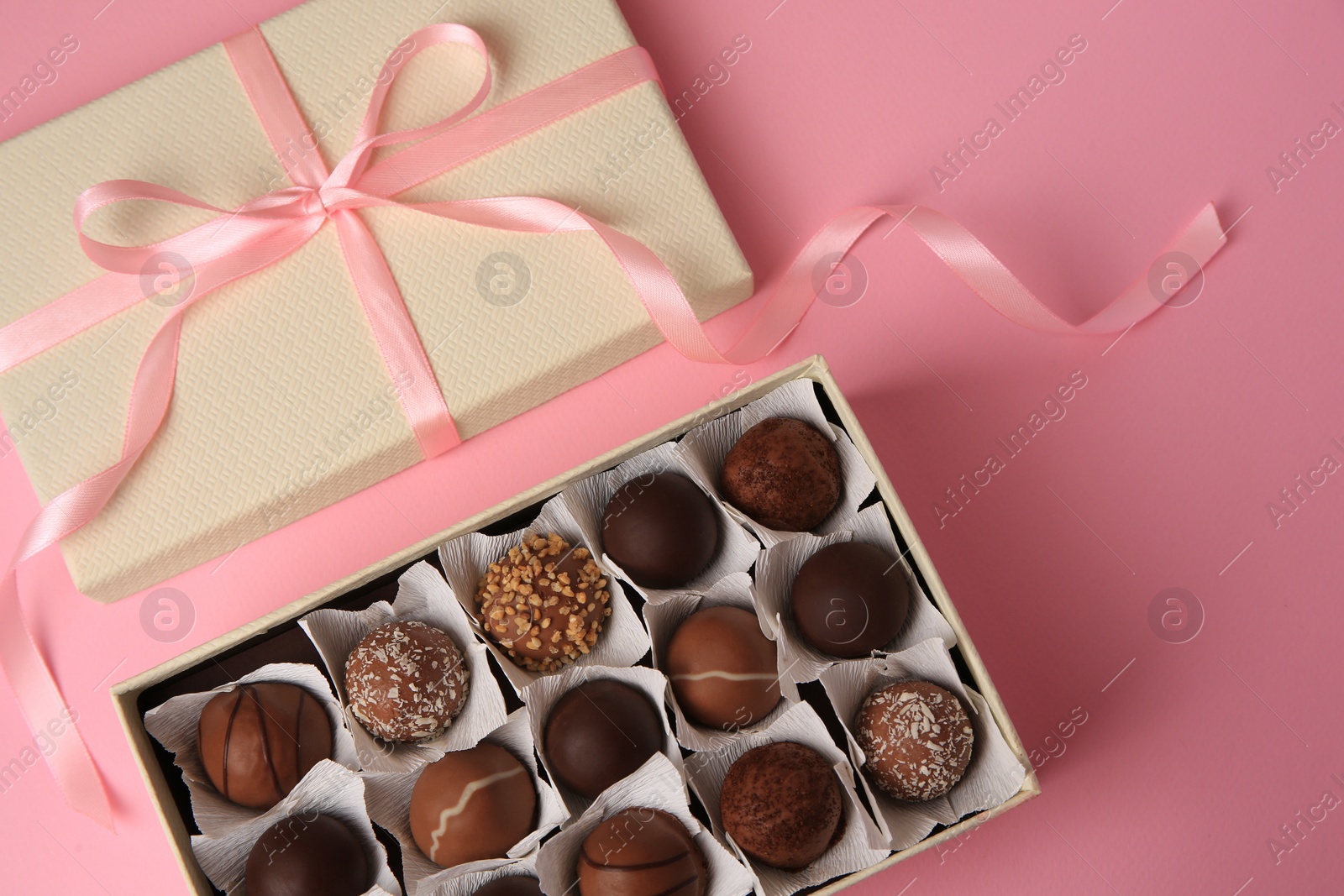 Photo of Box of delicious chocolate candies on pink background, flat lay