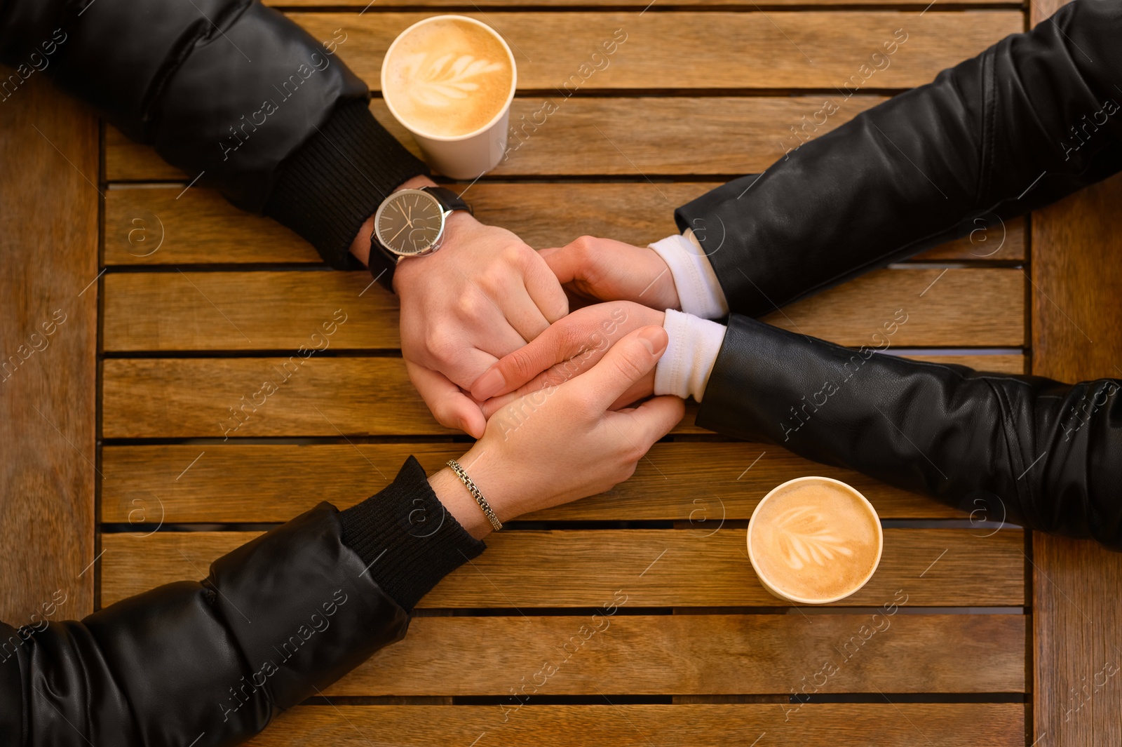 Photo of Lovely couple with coffee holding hands together at wooden table, top view. Romantic date