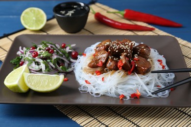 Pieces of soy sauce chicken with noodle, salad and lime served on blue table, closeup