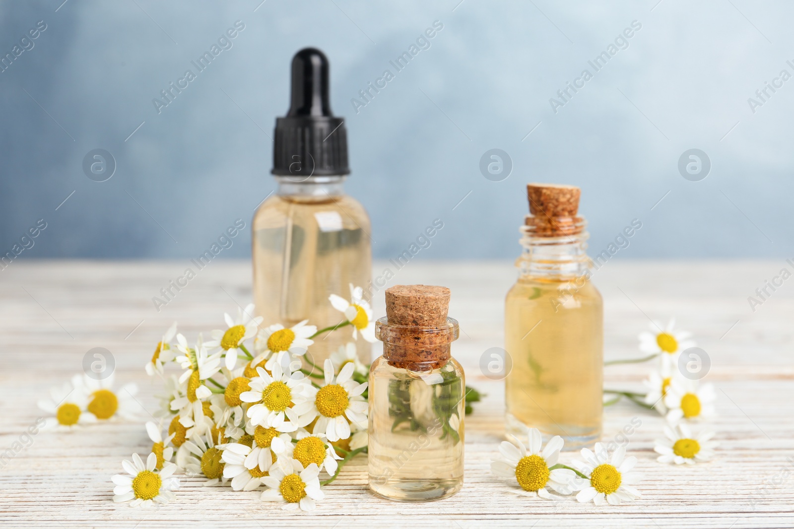 Photo of Bottles of essential oil and chamomiles on white wooden table