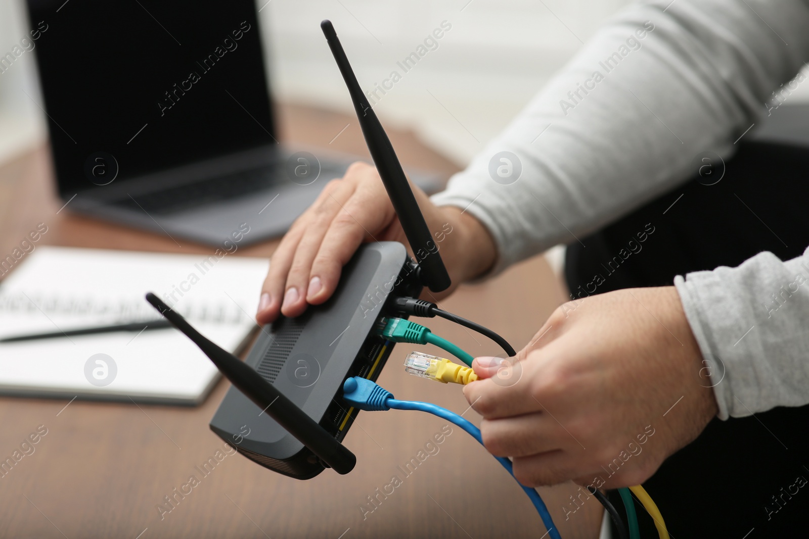 Photo of Man inserting cable into Wi-Fi router at wooden table indoors, closeup