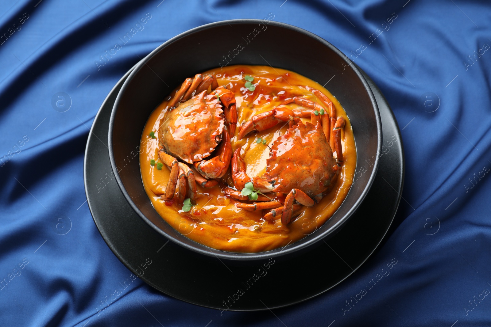 Photo of Delicious boiled crabs with sauce in bowl on blue tablecloth