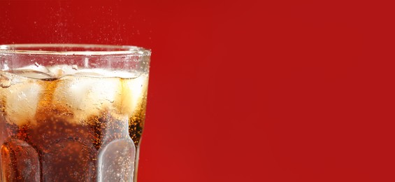 Image of Tasty refreshing soda drink with ice cubes on red background, closeup. Banner design with space for text