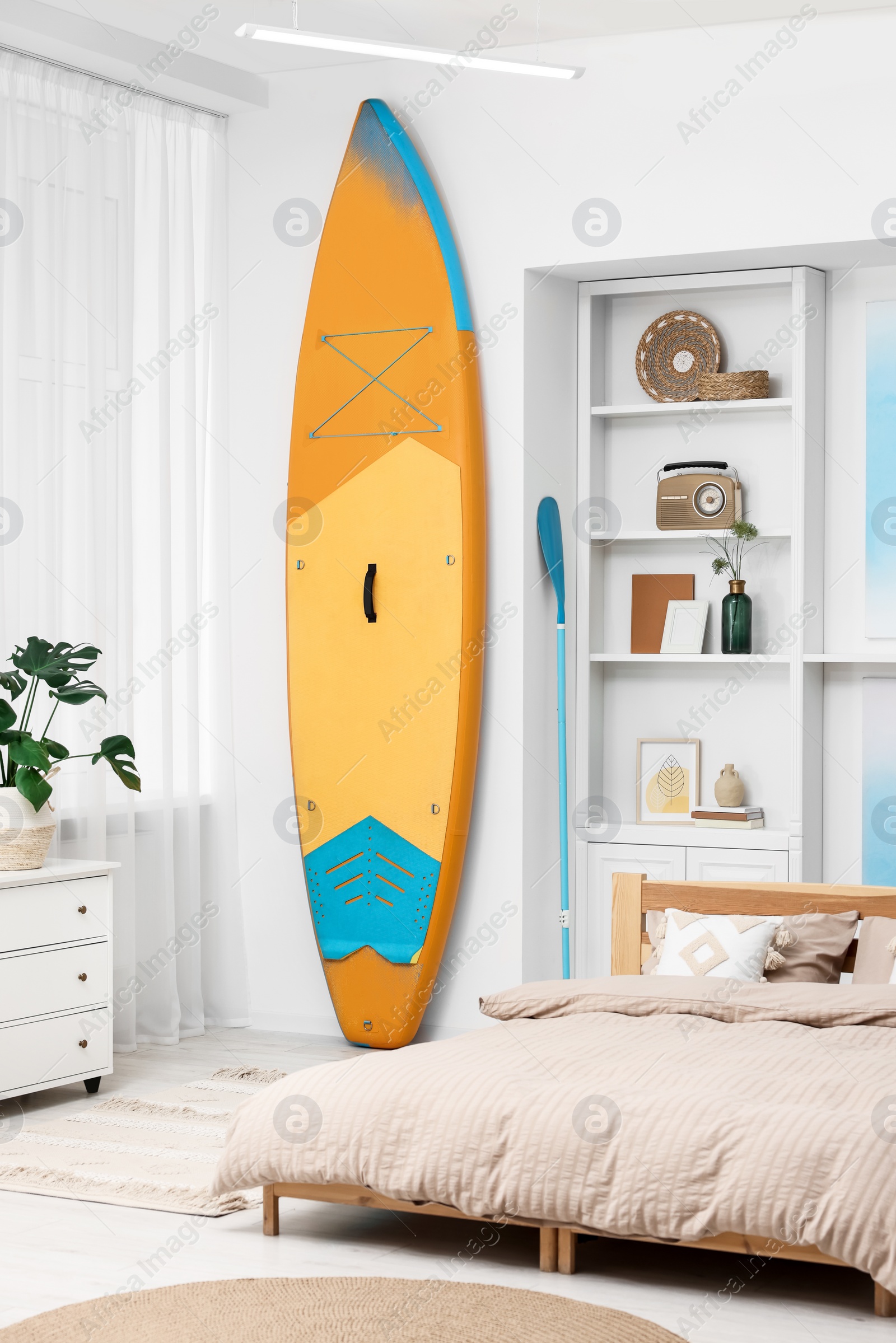 Photo of SUP board, bed and furniture in room. Interior design