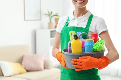 Woman with basin of detergents in living room, closeup. Cleaning service