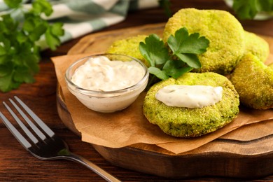 Photo of Tasty vegan cutlets served with sauce and parsley on wooden table, closeup