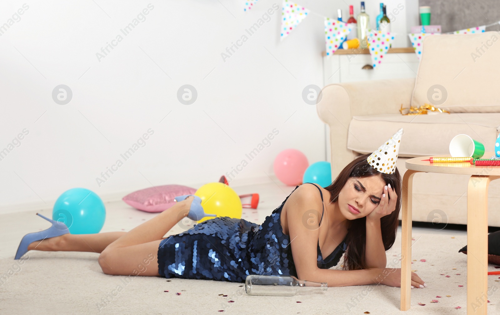 Photo of Young woman suffering from hangover in messy room after party