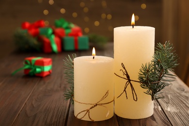 Burning candles with fir branches on wooden table against blurred background, space for text