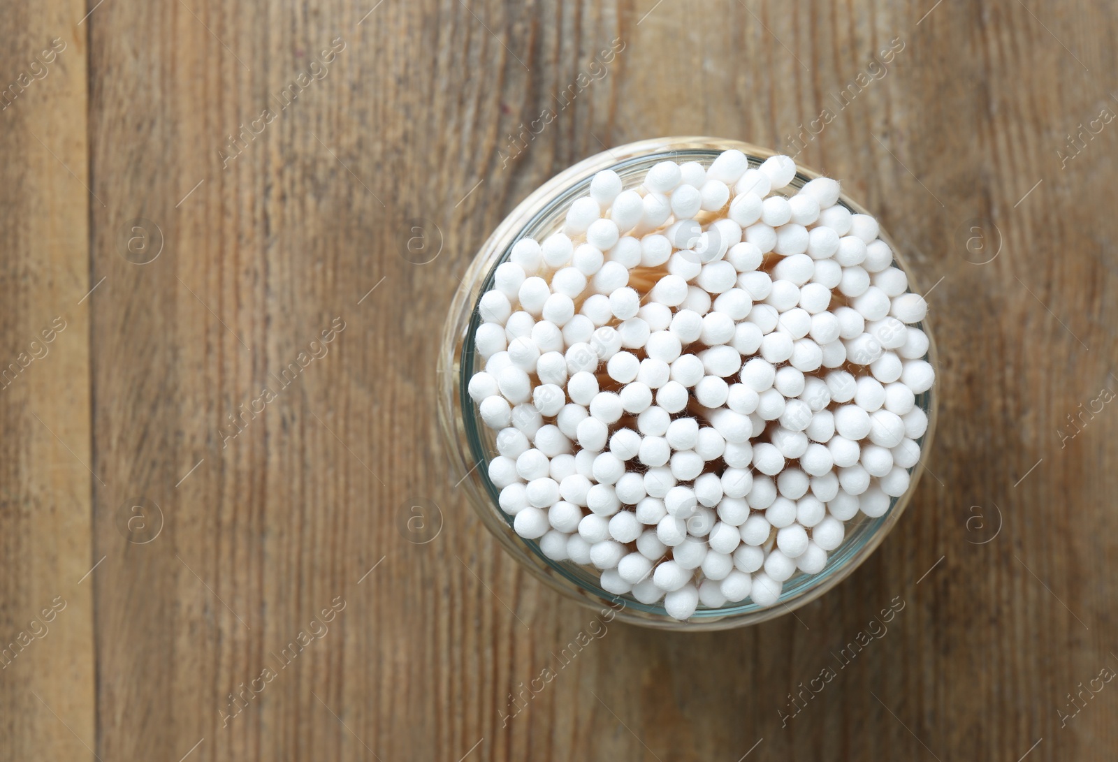 Photo of Many cotton buds in glass jar on wooden table, top view. Space for text