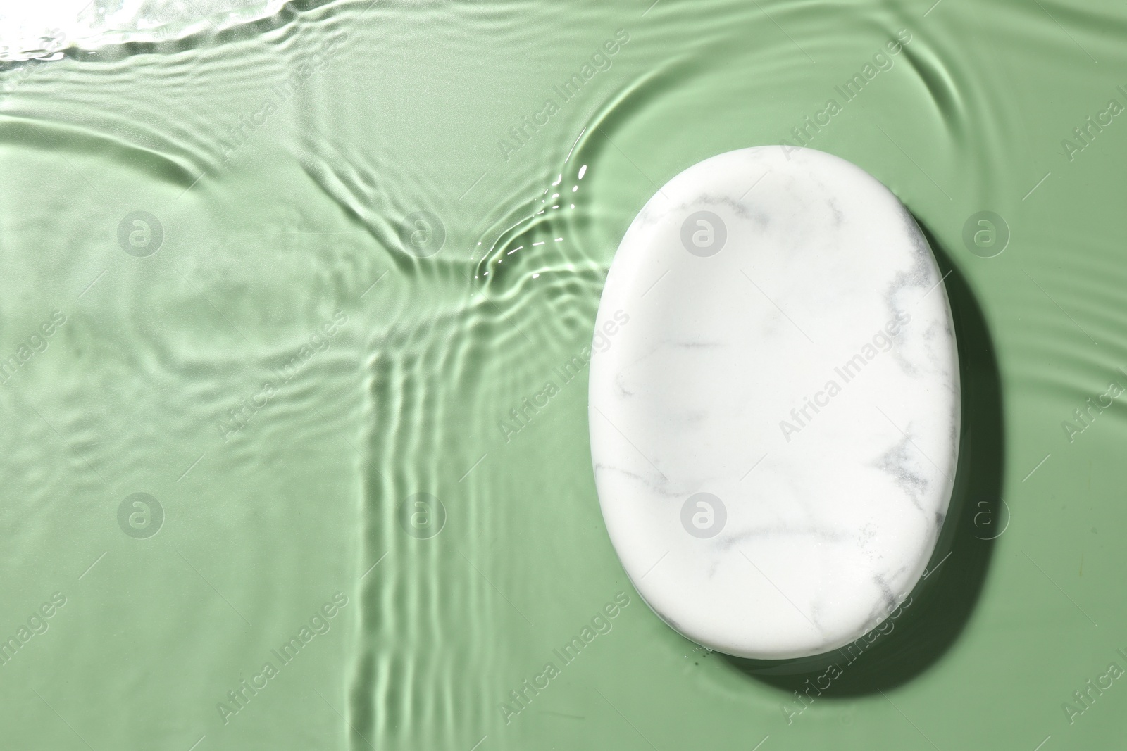 Photo of Presentation of product. Marble podium in water on green background, top view. Space for text