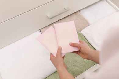 Photo of Woman putting scented sachets into drawer with towels, closeup