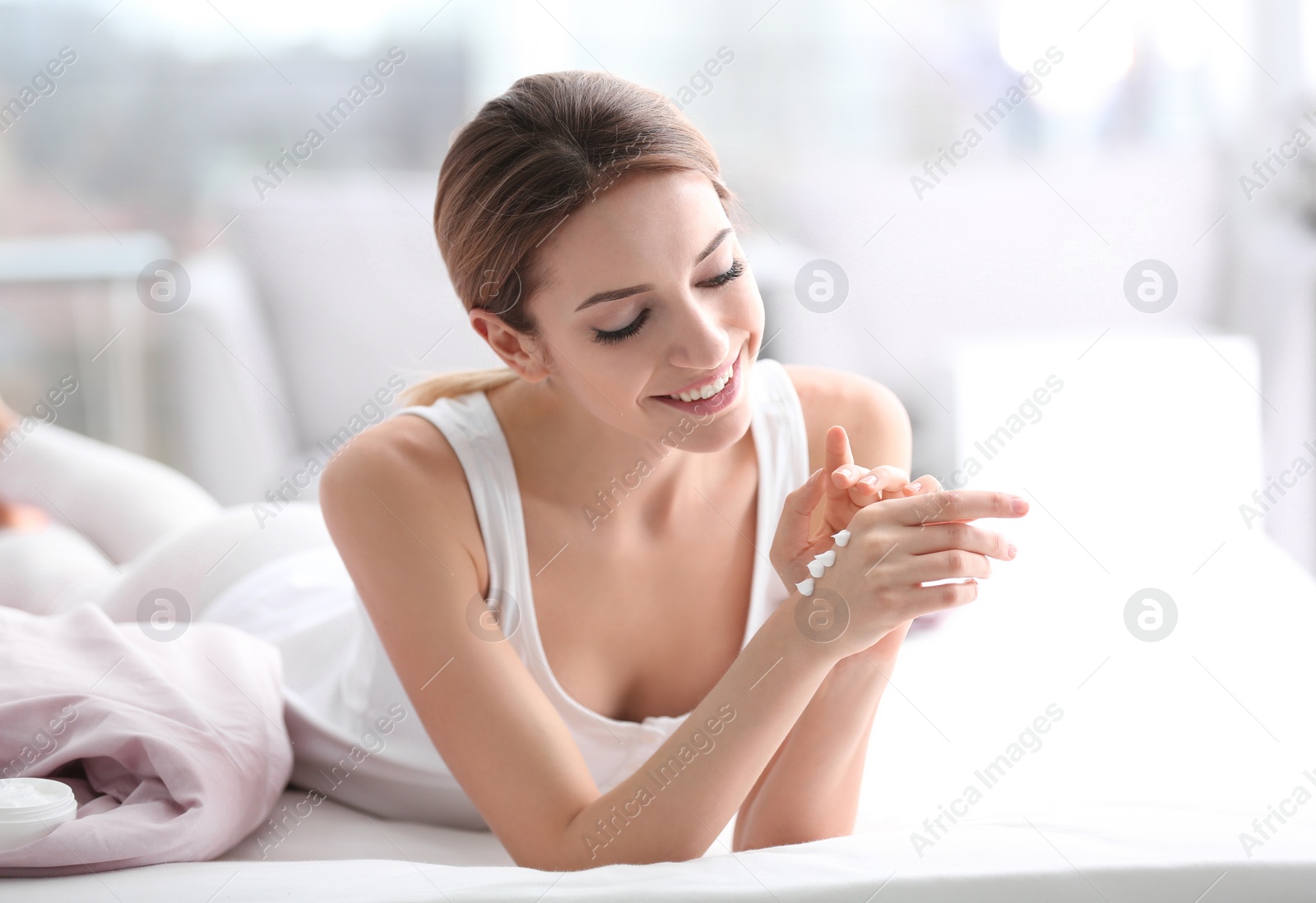 Photo of Young woman applying hand cream on bed at home