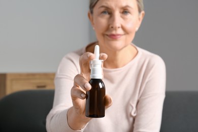 Photo of Woman holding nasal spray indoors, focus on bottle