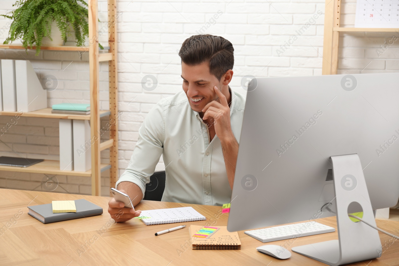 Photo of Handsome man using smartphone while working with calendar at table in office