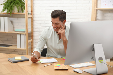 Handsome man using smartphone while working with calendar at table in office