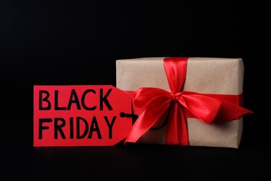 Photo of Gift box and tag with words Black Friday on dark background