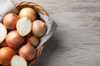 Photo of Wicker basket with whole and cut onions on light grey wooden table, top view. Space for text