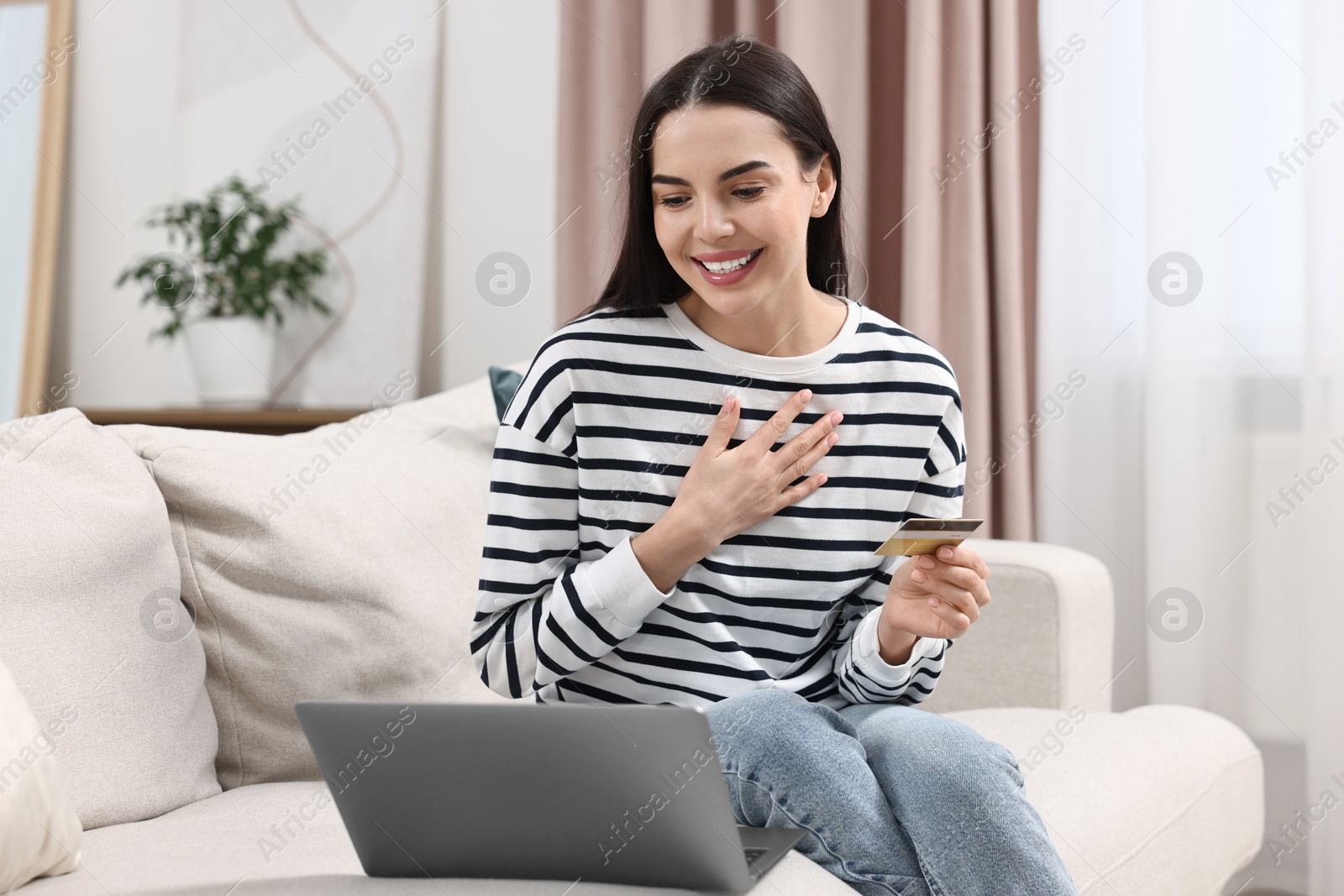 Photo of Happy young woman with credit card and laptop shopping online at home