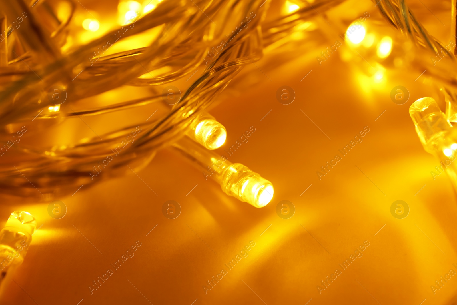 Photo of Glowing Christmas lights on yellow background, closeup