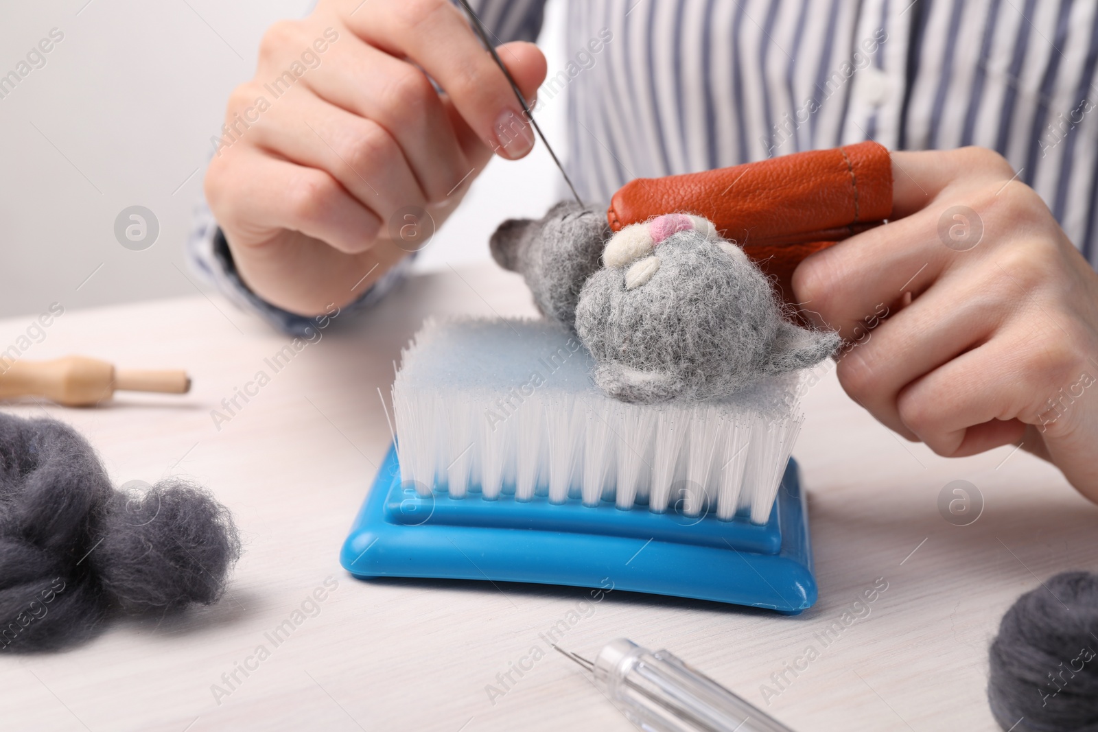 Photo of Woman felting toy cat from wool at light wooden table, closeup