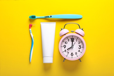 Photo of Toothpaste, toothbrushes and alarm clock on yellow background, flat lay