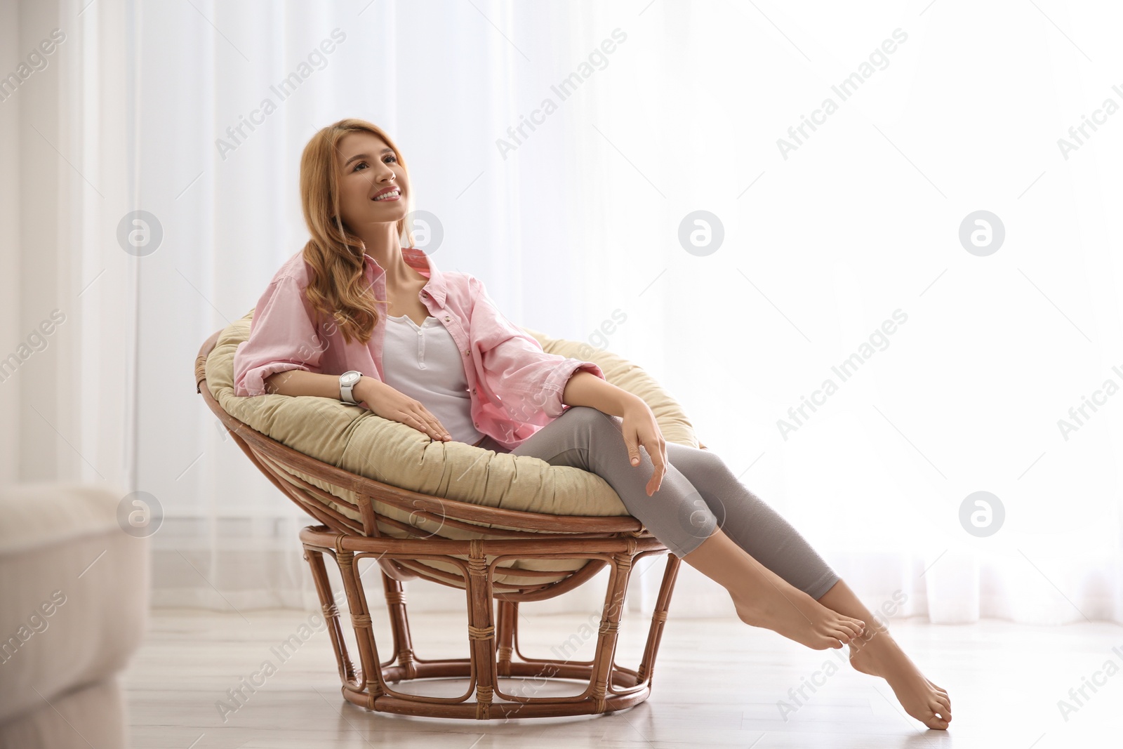 Photo of Young woman relaxing in papasan chair near window at home