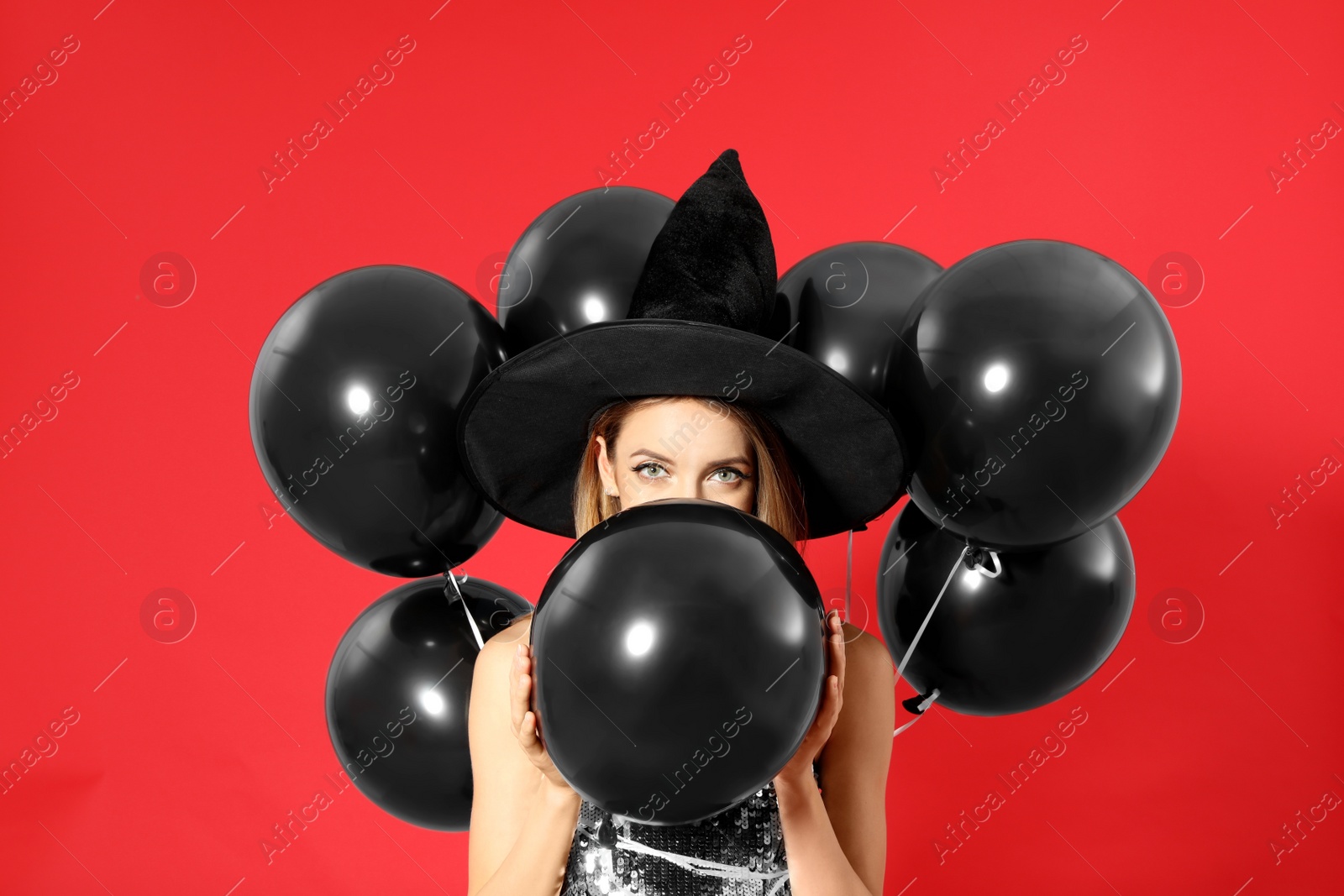 Photo of Beautiful woman wearing witch costume with balloons for Halloween party on red background