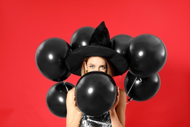 Beautiful woman wearing witch costume with balloons for Halloween party on red background