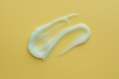 Photo of Sample of face cream on yellow background, top view