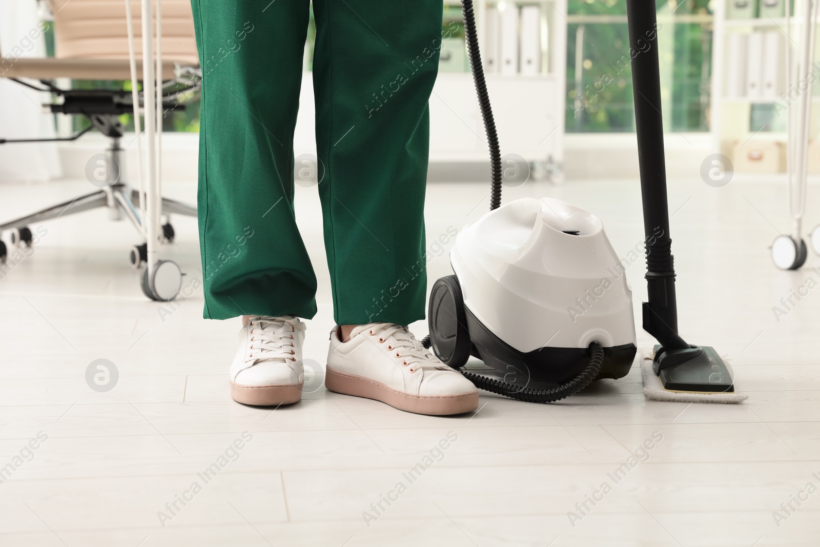 Photo of Janitor and professional steam cleaner indoors, closeup