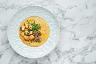 Photo of Delicious cream soup with mushrooms and croutons on white marble table, top view. Space for text