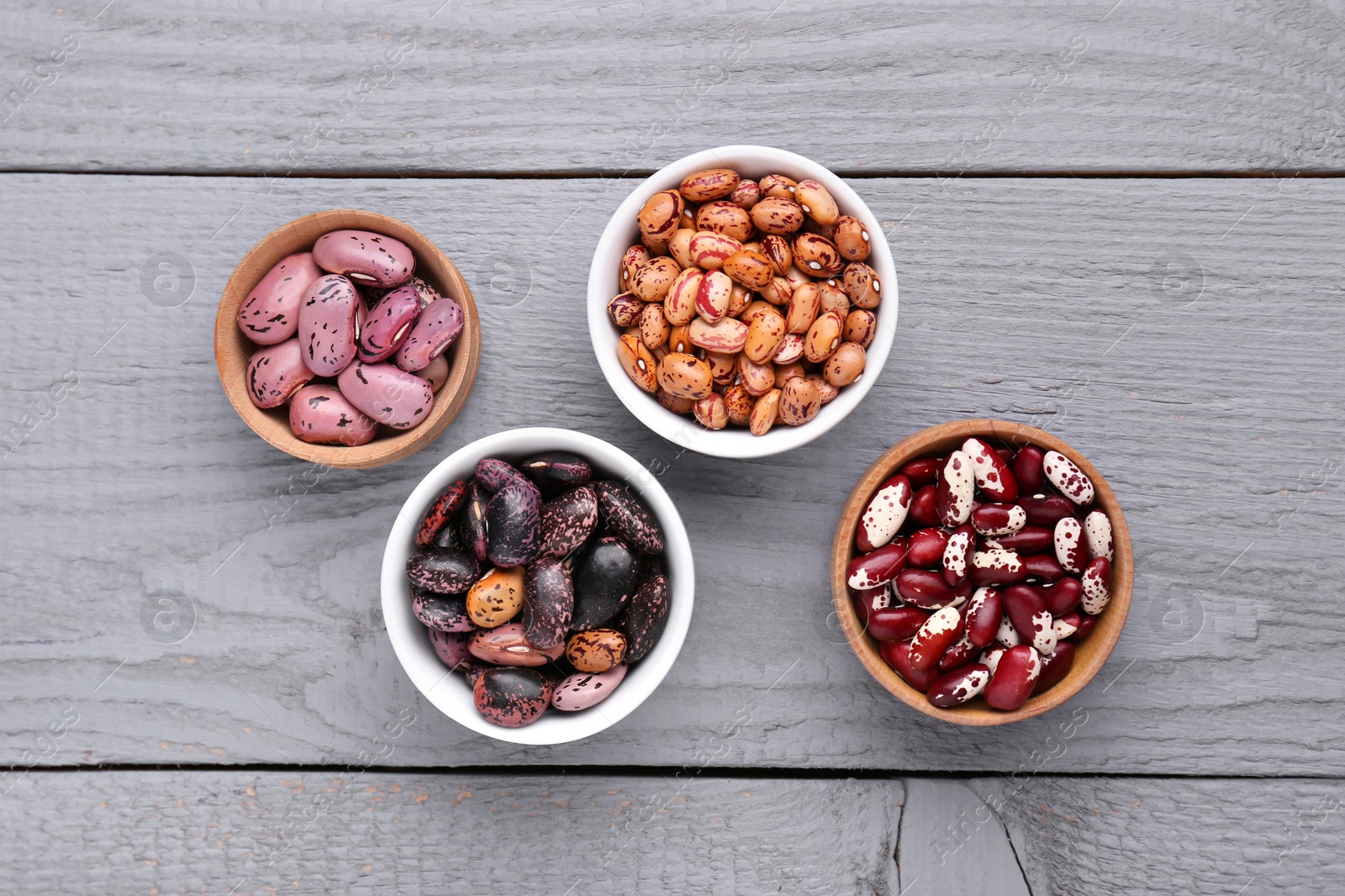 Photo of Different kinds of dry kidney beans on light grey wooden table, flat lay