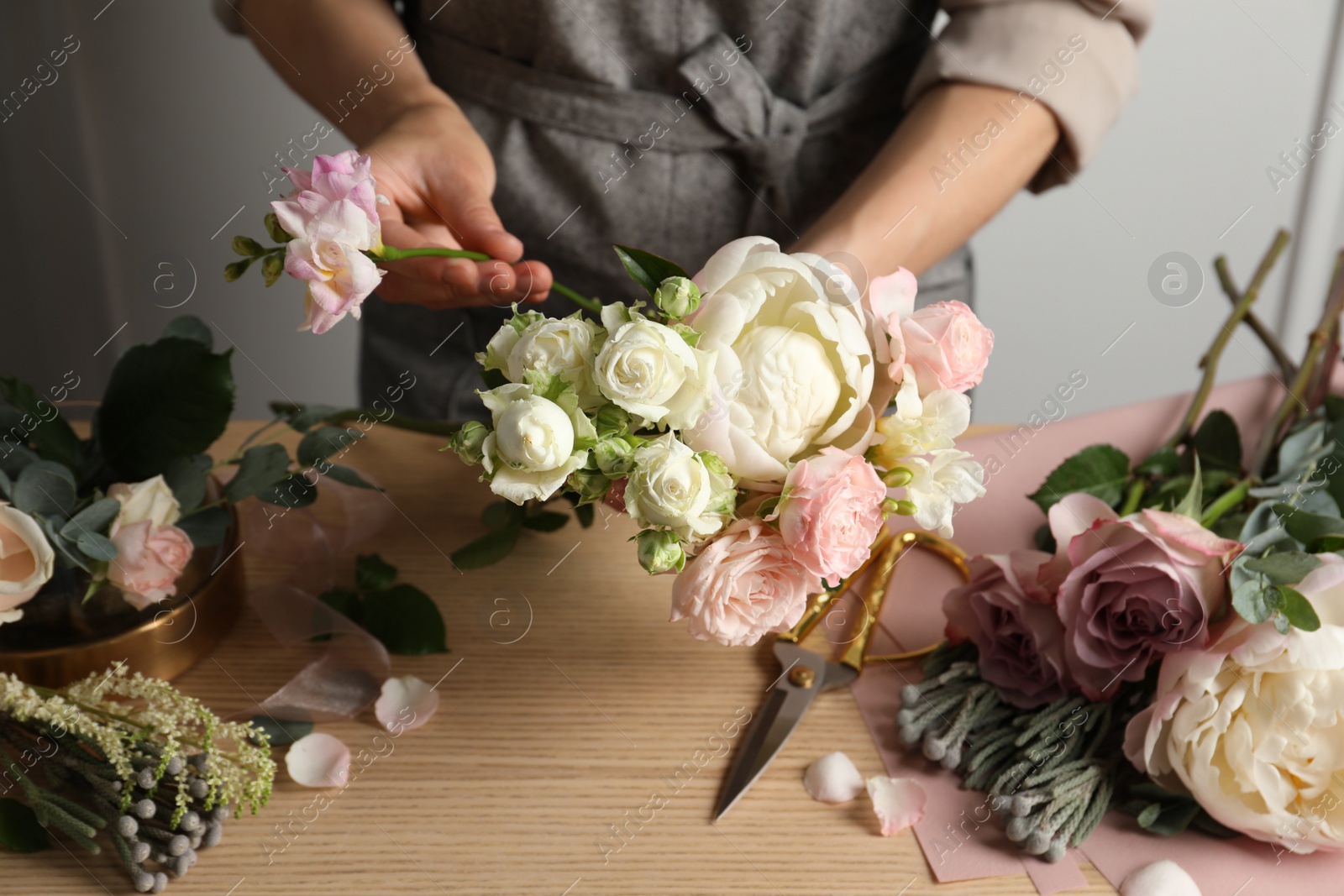 Photo of Florist creating beautiful bouquet at wooden table indoors, closeup