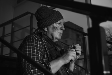 Photo of Poor senior man with bread on stairs indoors. Black and white effect