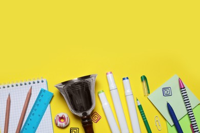 Photo of Different stationery and school bell on yellow background, flat lay. Space for text